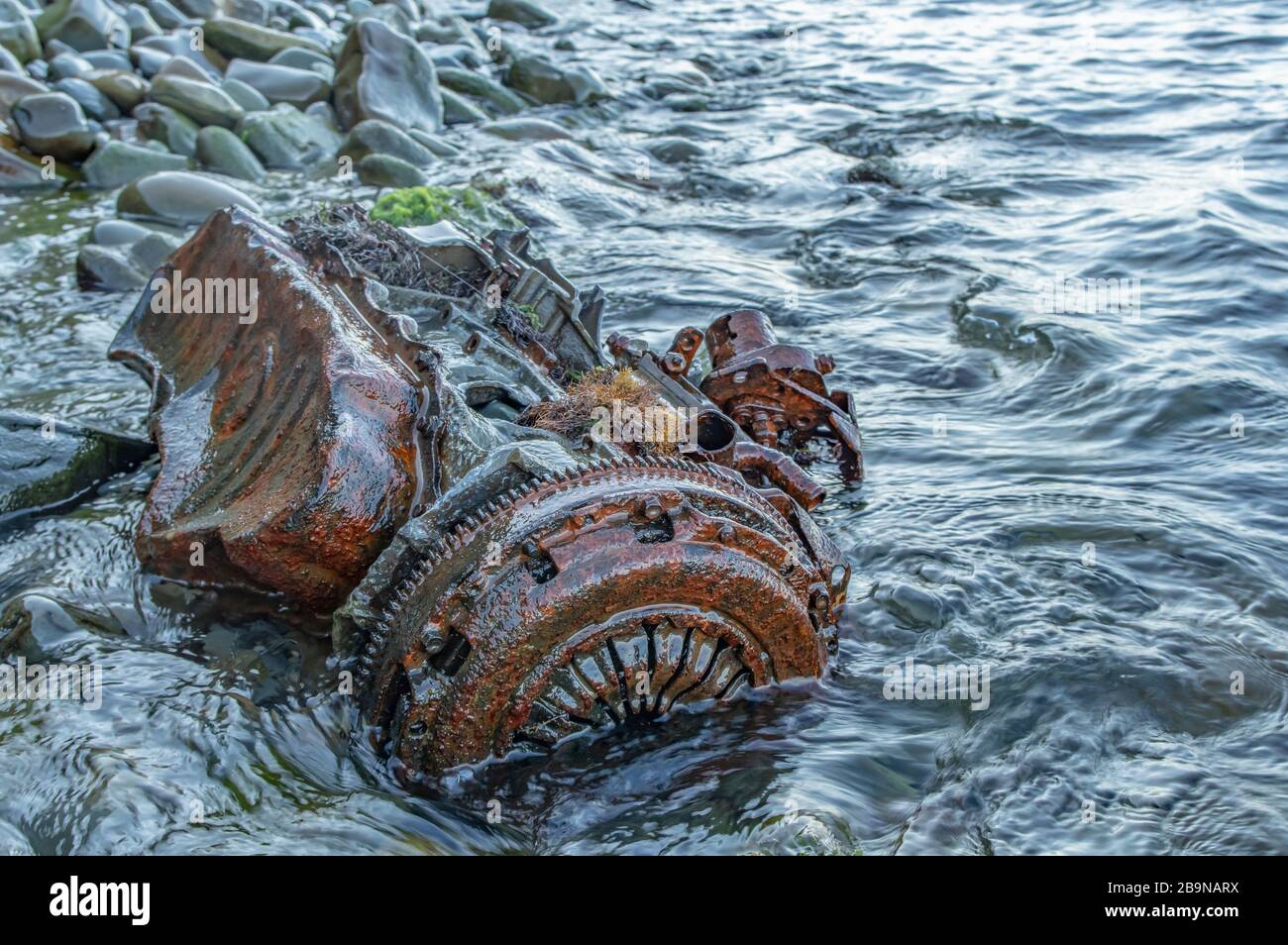 Alter rostiger Motor, der unter Steinen im Wasser liegt. Stockfoto