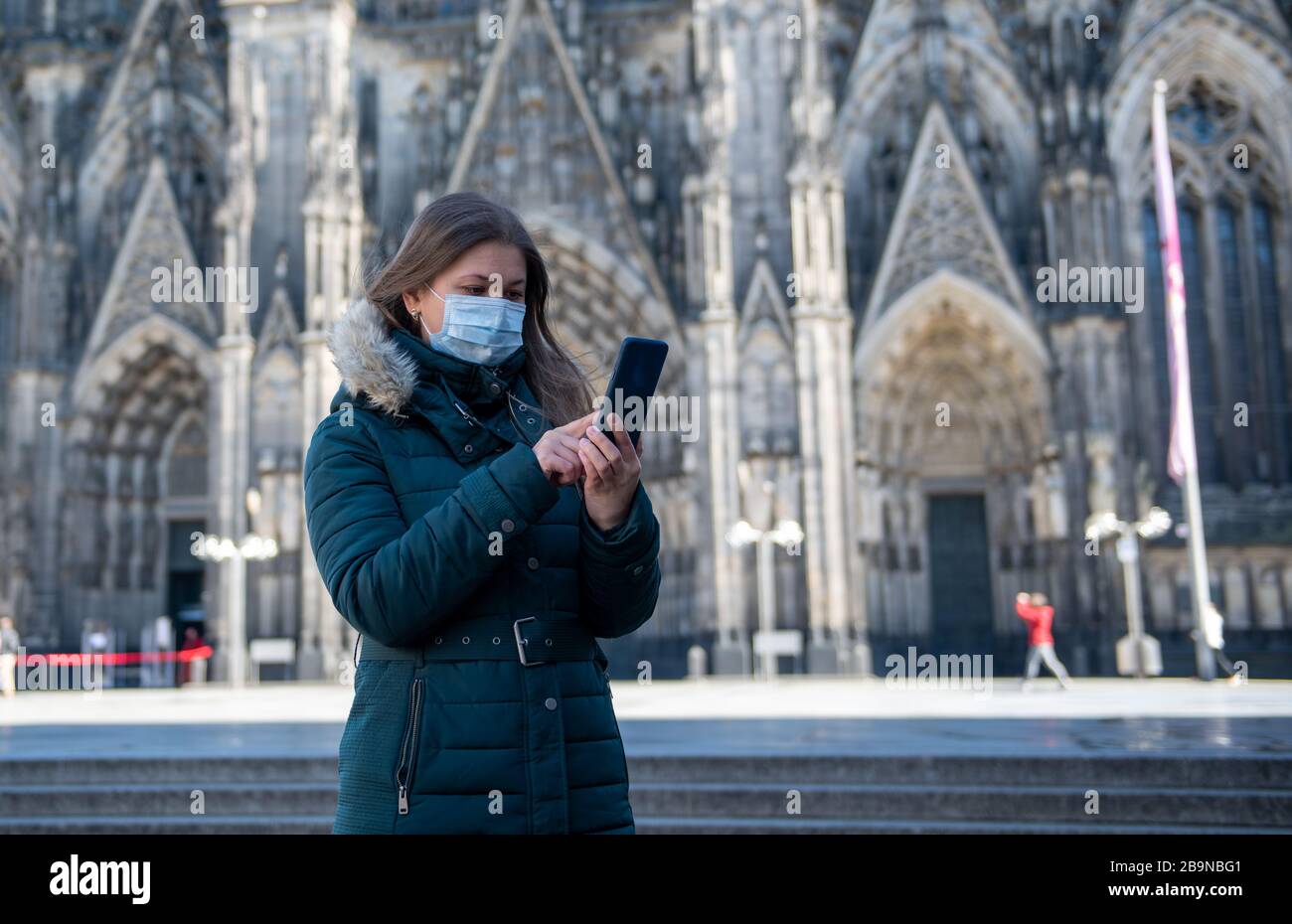 Junge Frau mit ärztlicher Schutzmaske unter Quarantäne von Coronavirus (COVID-19) mit Smartphone vor dem Kölner Dom in Deutschland, Europa Stockfoto