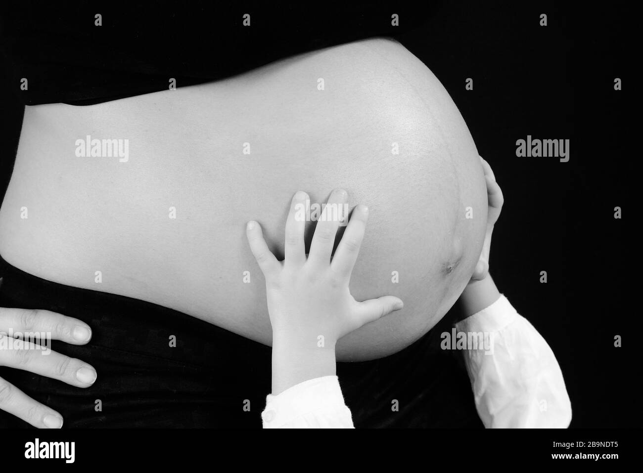 Schwarz-weißes Bild des Bauch einer schwangeren Frau mit kleinen Händen unterstützt. Stockfoto