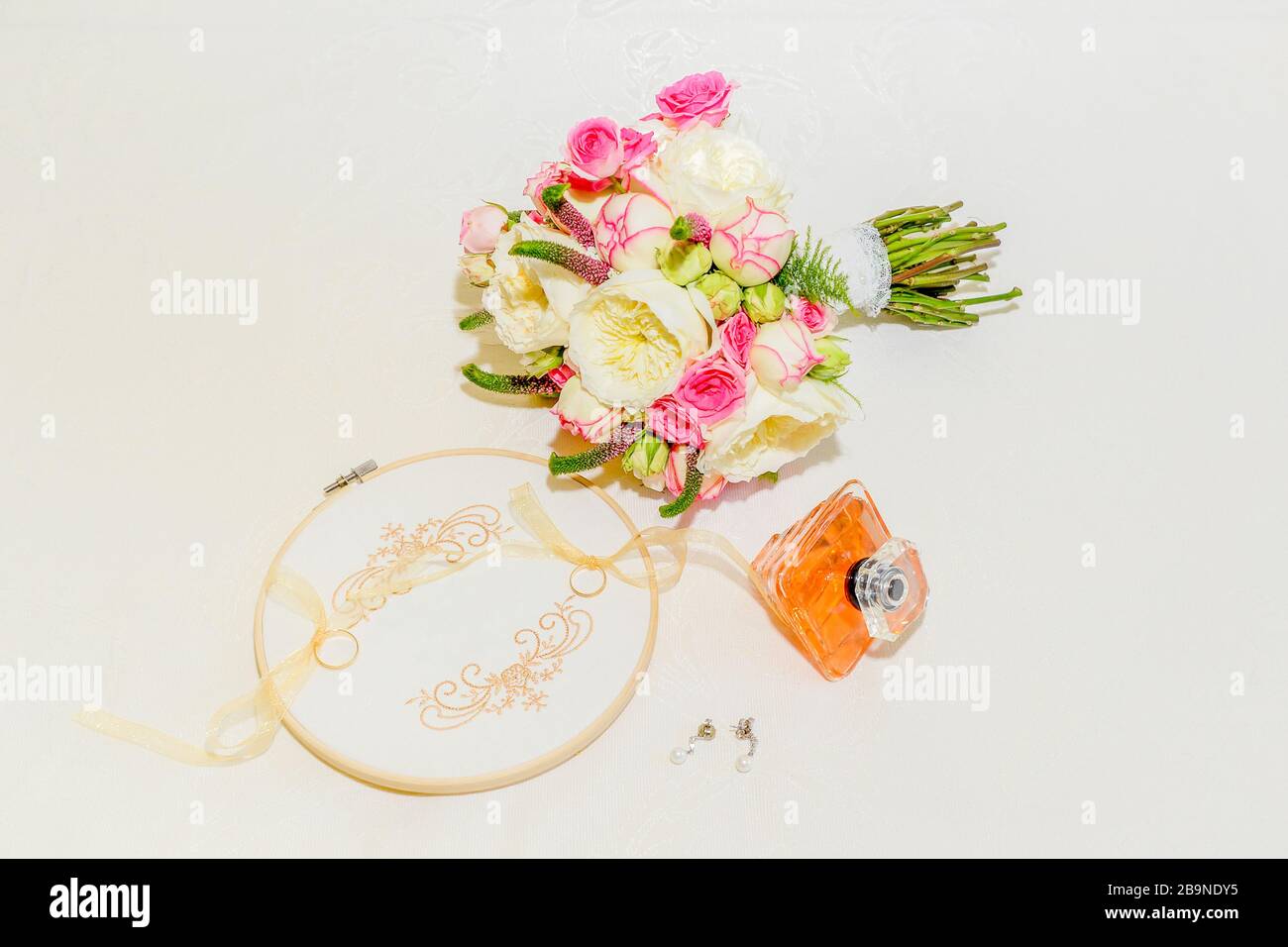 Strauß Rosen und weiße und rosa Pfingstrosen neben Rahmen mit Ringen, Ohrringen und Duft einer Braut Stockfoto