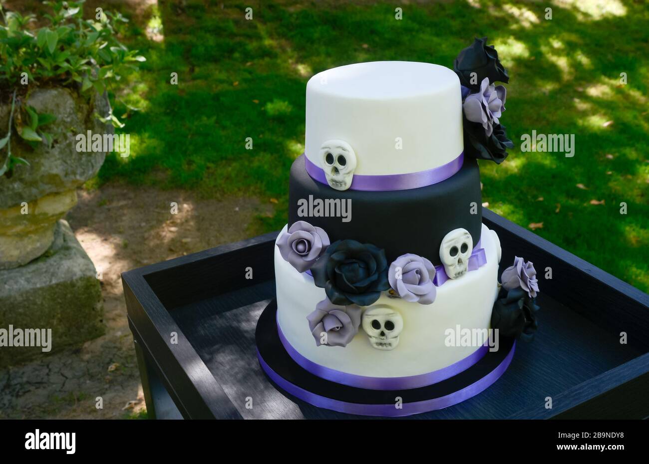 Schöne Brautkuchen in weiß, schwarz und lila mit Blumen und Schädeln verziert Stockfoto