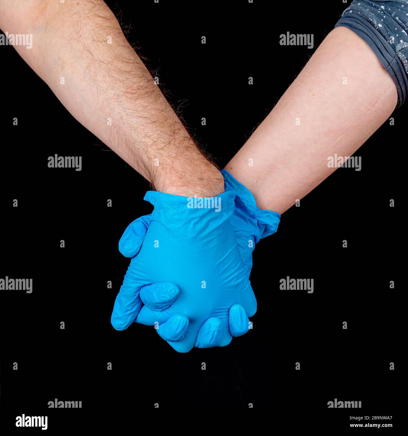 Ein Paar hält die Hände, während es blaue Latexhandschuhe trägt. Nahansicht mit nur den Händen. Schwarzer Hintergrund. Stockfoto