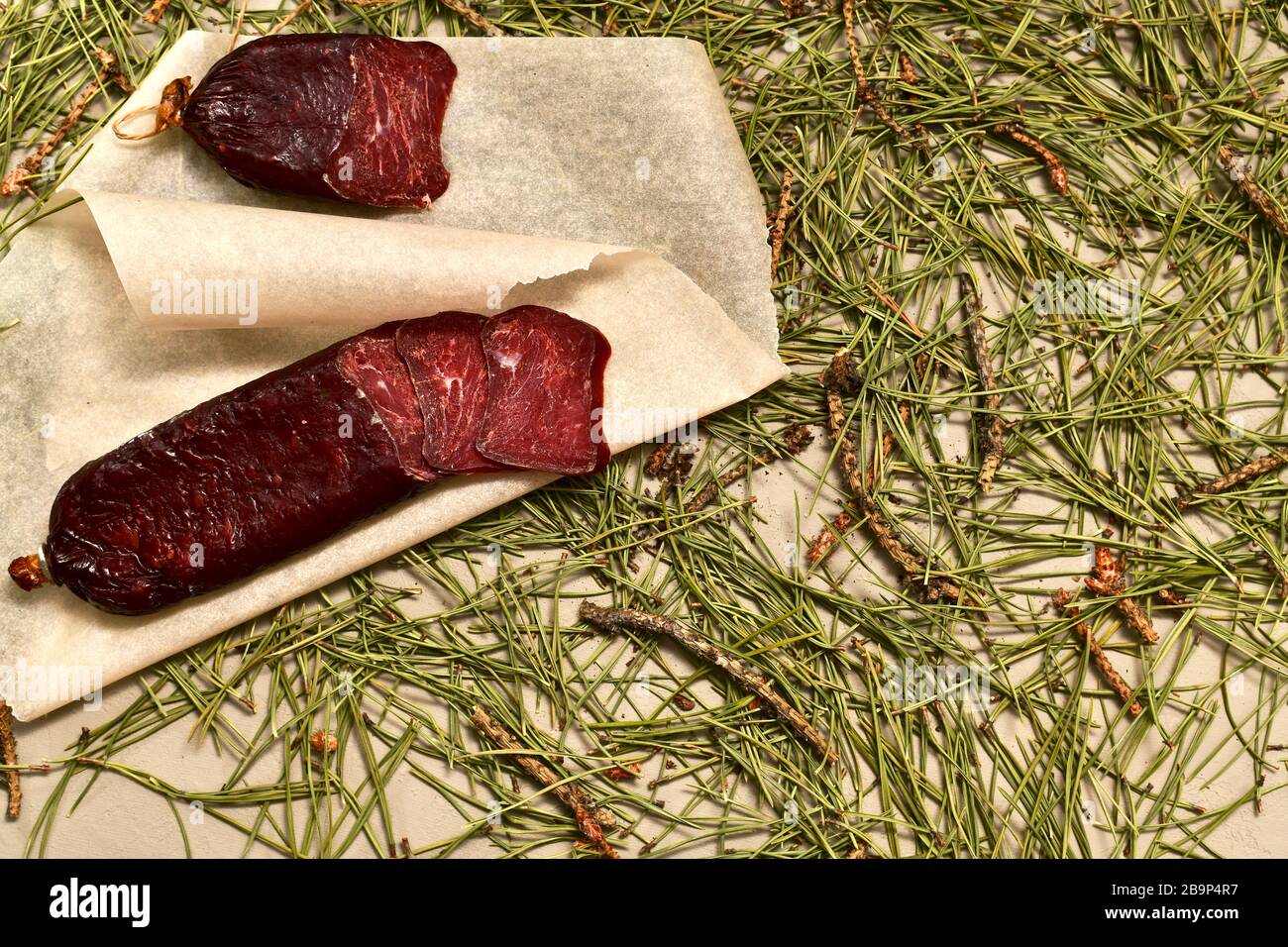 Getrocknete Wurst aus Rehe. Schneiden Sie mit Scheiben auf Pergament, einem großen Fragment. Bodenbelag aus Kiefernnadeln. Stockfoto