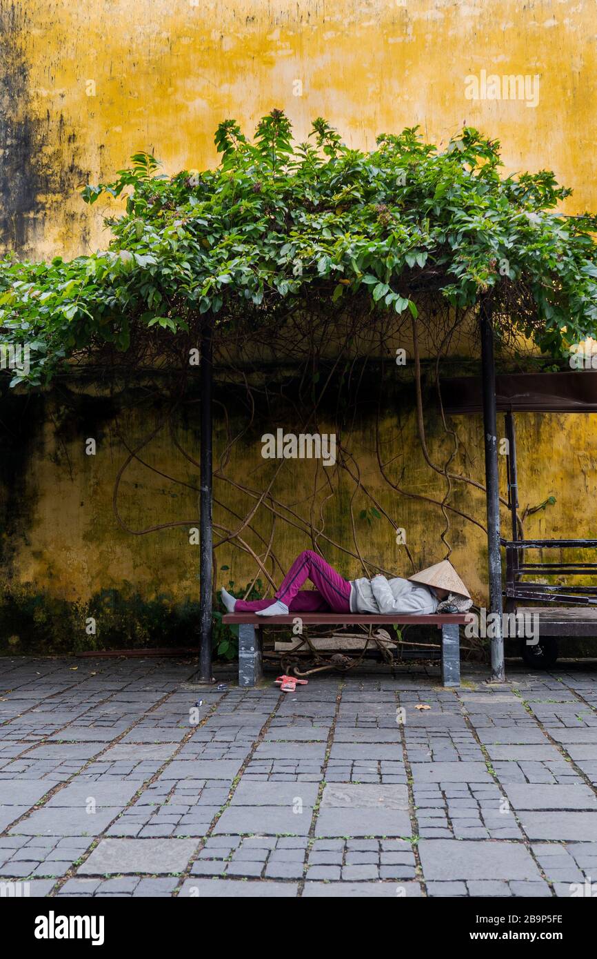 Eine Person, die auf der Bank in Hoi an schläft, mit den berühmten gelben Wänden auf dem Hintergrund, ein Straßenfoto aus Vietnam. Stockfoto