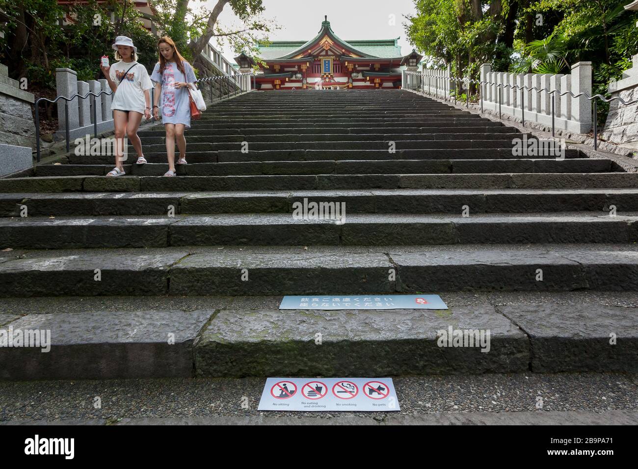 Chinesische Touristen auf Stufen am Hie-Schrein mit Schildern, die Besucher vor den Regeln des Schreins warnen. Hie-Schrein, Nagatacho, Tokio, Japan. Stockfoto
