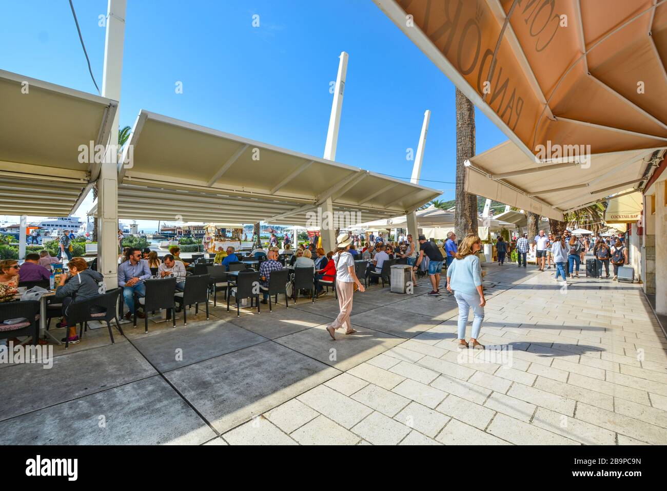 Touristen genießen ein Cafe an einem sonnigen Tag an der Uferpromenade Riva am Hafen entlang der Adria an der Küste Dalmatiens Split, Kroatien Stockfoto
