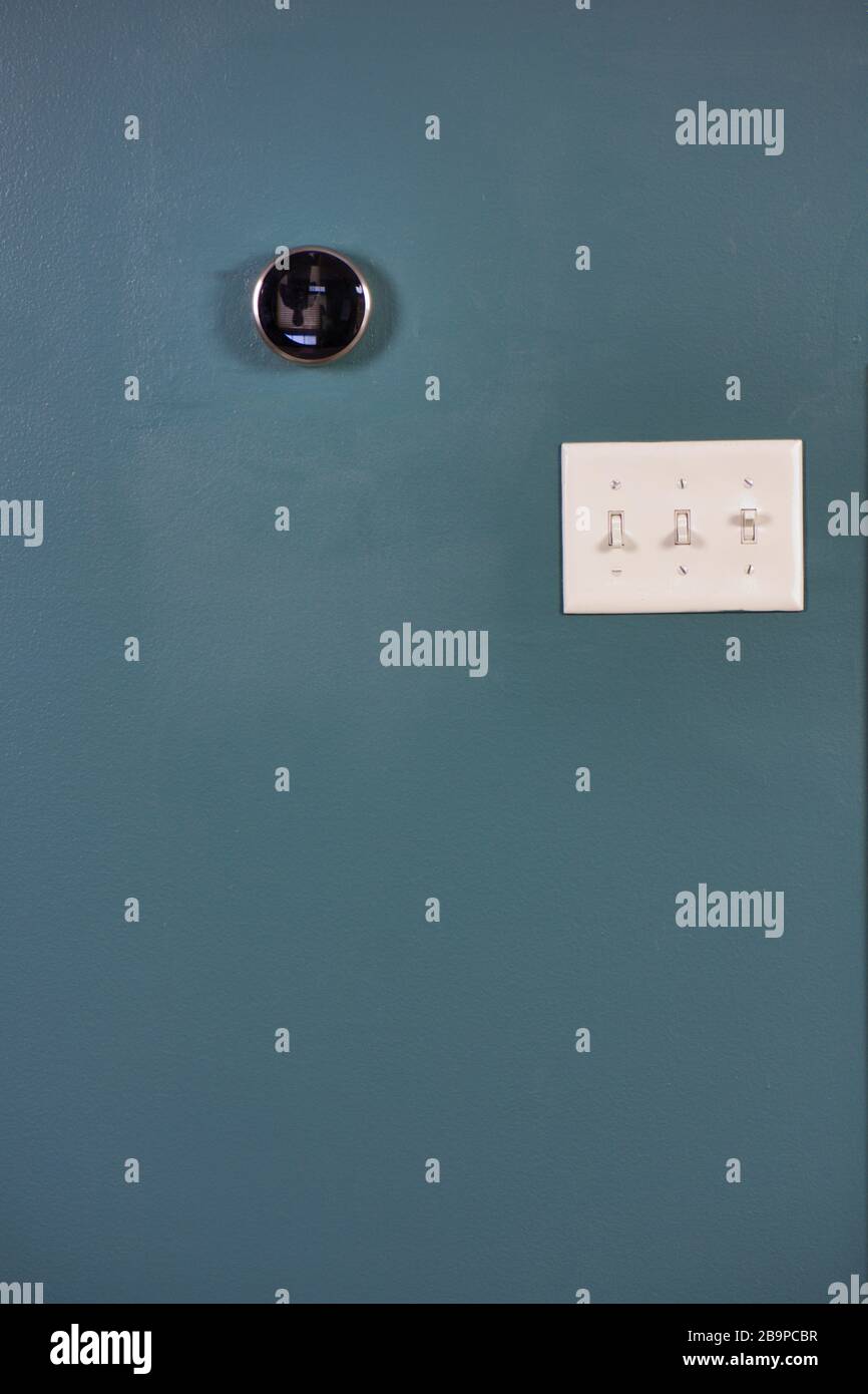 Smart Home Thermostat an blauer Wand mit Lichtschalter isoliert. Mehrere Möglichkeiten, Geld und Energie zu sparen. Stockfoto