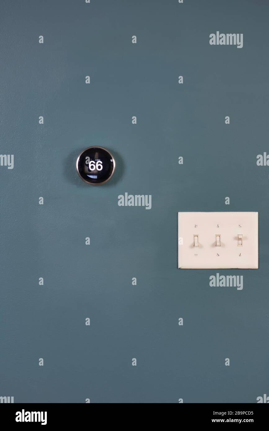 Smart Home Thermostat an blauer Wand mit Lichtschalter isoliert. Mehrere Möglichkeiten, Geld und Energie zu sparen. Stockfoto