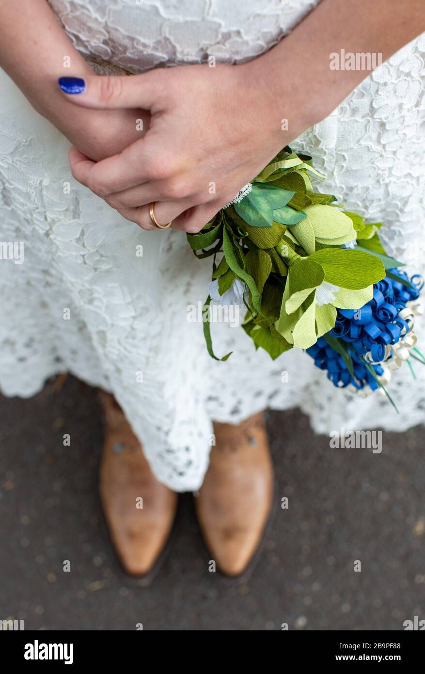 Eine andere Frau, die Cowboystiefel trägt und hausgemachtes Blumenstrauß aus Papier hält Stockfoto