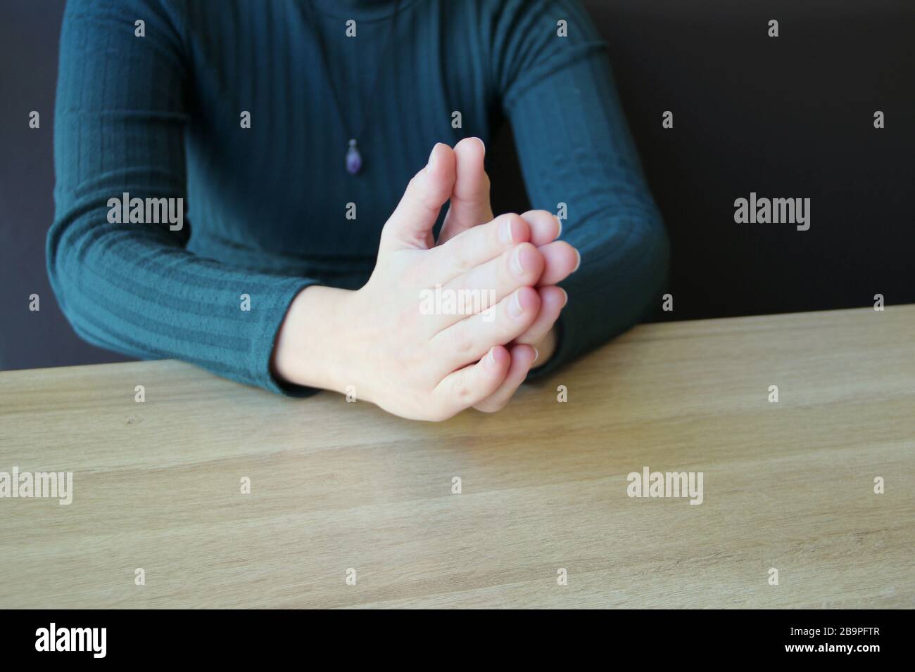 Im Gebet gefaltete Handflächen. Das Mädchen sitzt und hält die Hände vor den zusammengeklemmten Händen. Stockfoto