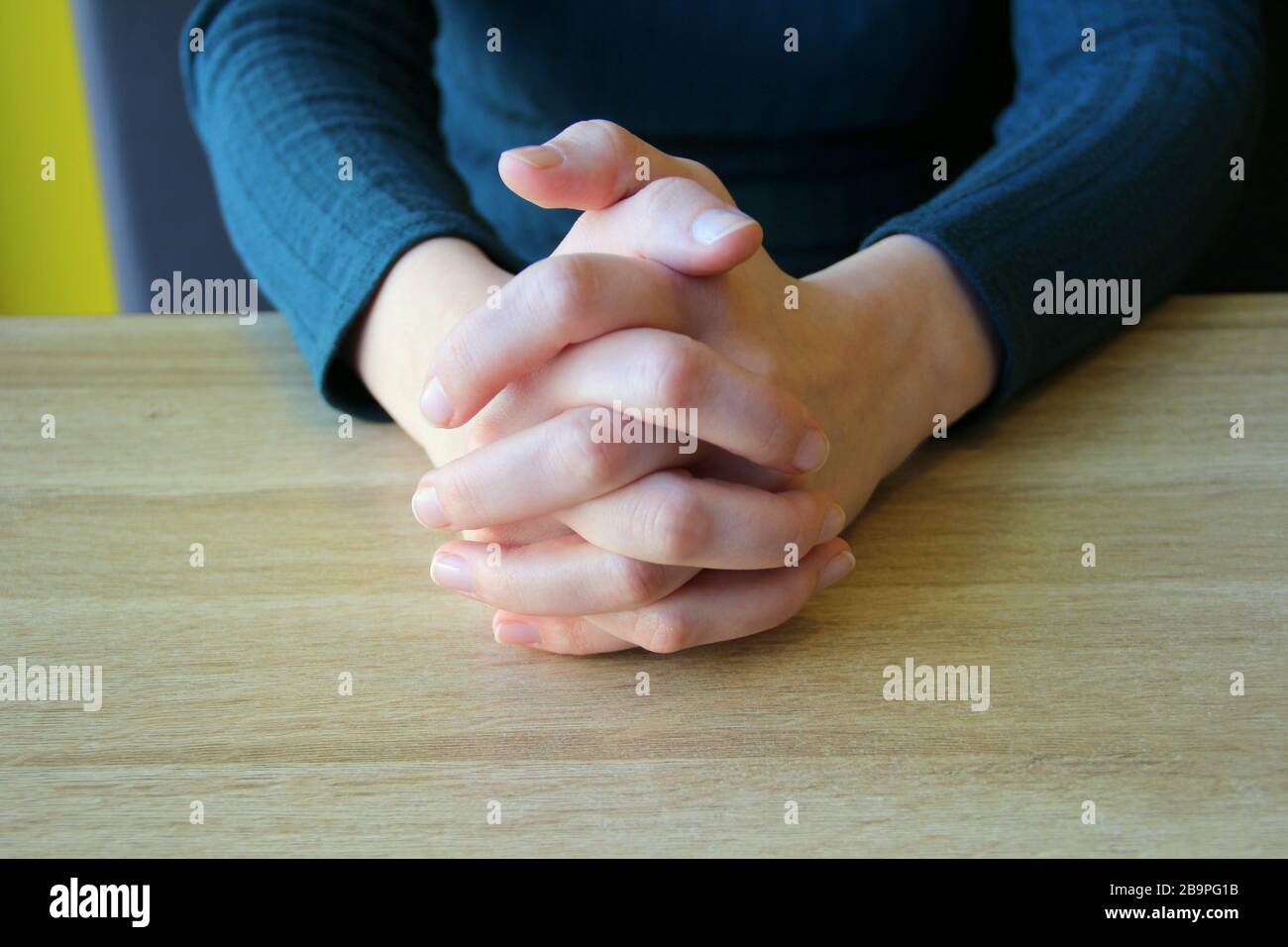 Im Gebet gefaltete Handflächen. Eingeklemmte Finger. Das Mädchen sitzt und hält die Hände vor den zusammengeklemmten Händen. Stockfoto