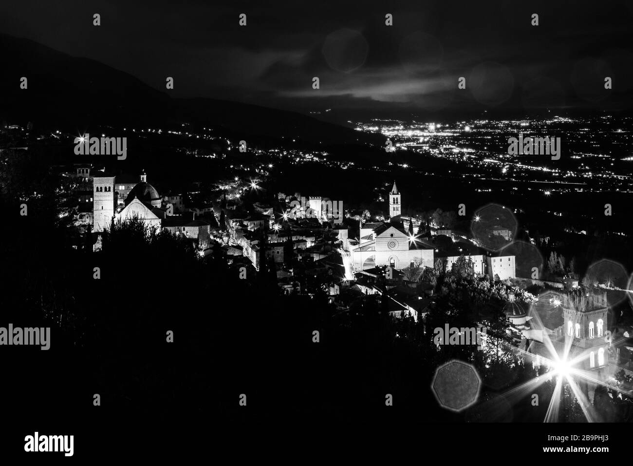 Blick auf die Stadt Assisi (Umbrien, Italien) und das Tal bei Nacht, mit Stadtbeleuchtung und Kirche Santa Chiara Stockfoto