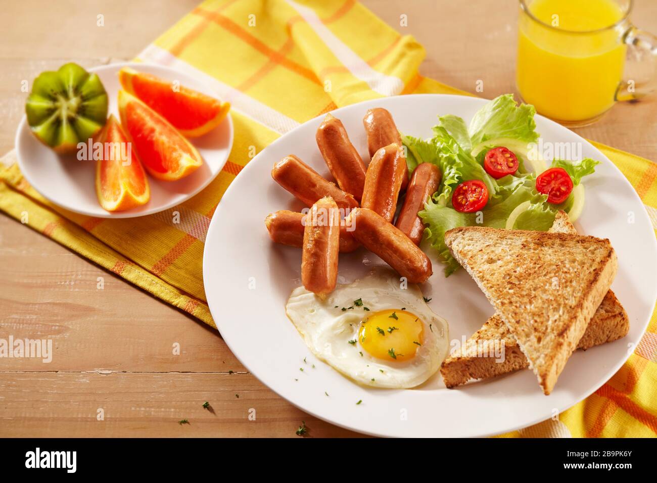 Ein Frühstücksplatte mit Cocktailwürsten, geröstetem Brot, Spiegeleiern, Salaten, Obst und einem Glas Orangensaft Stockfoto