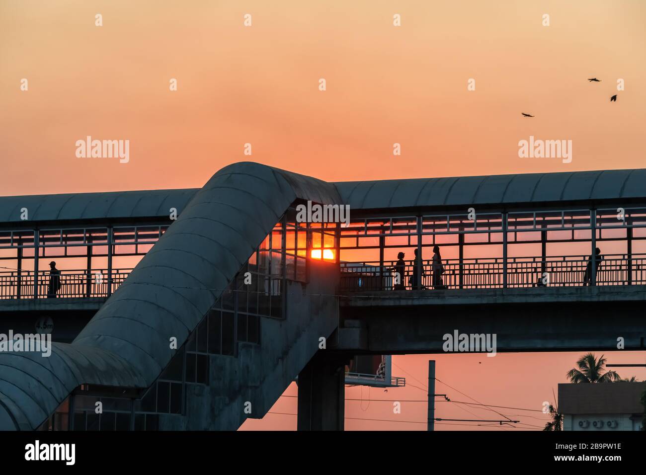 Die Menschen haben sich bei Sonnenuntergang über einer überschlägenden Brücke über eine belebte Straße in der Stadt getuschelt. Niedriger Winkel zur Pansodanbrücke mit unterer Sonne Stockfoto