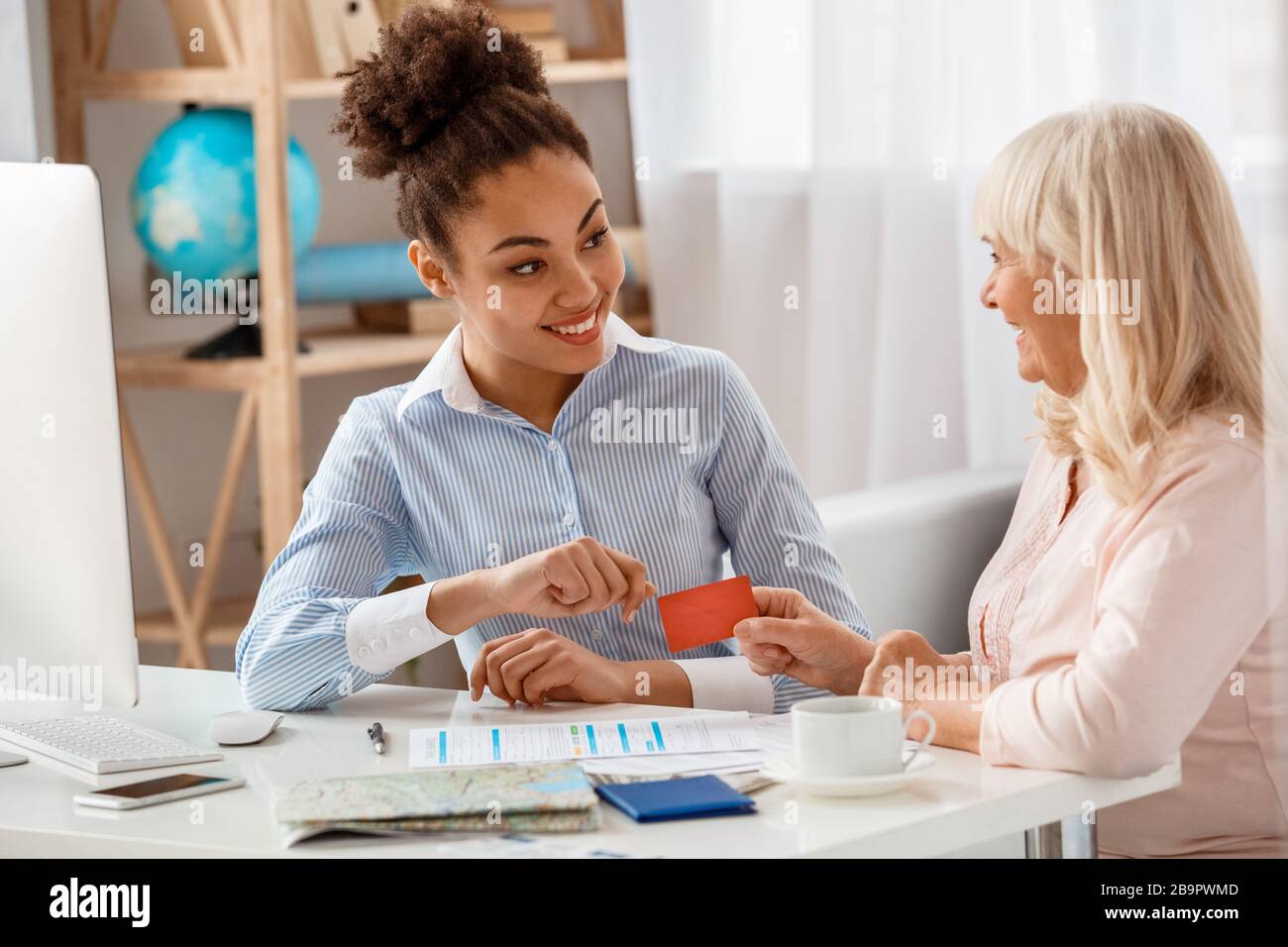 Reisebüro im Büro, das Debitkarte von einem älteren Kunden nimmt, ist freundlich Stockfoto