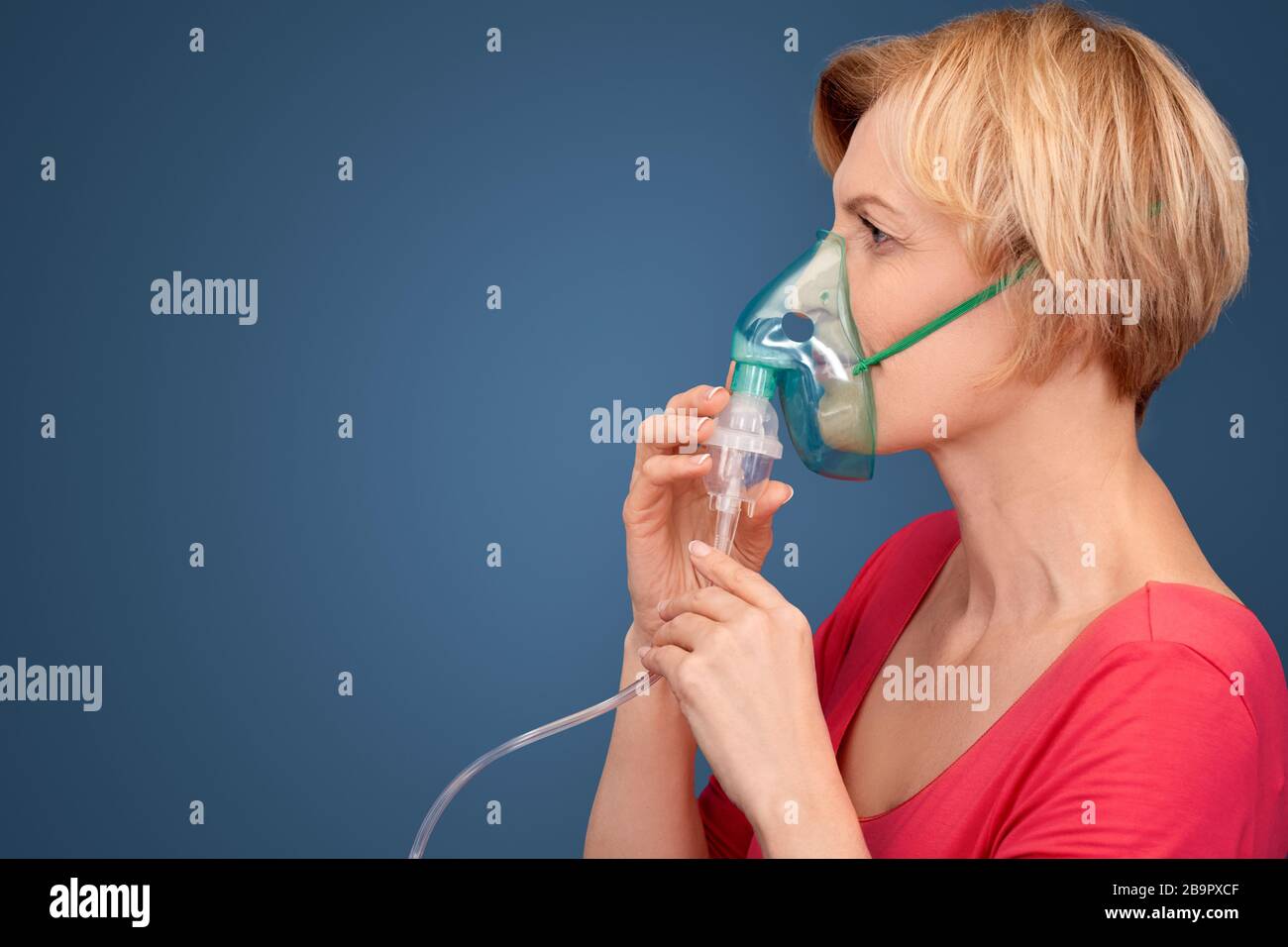 Coronavirus-Konzept. Blonde Frau in Oxigen Maske stehend isoliert auf blau nachdenkliche Kopie Raum Seitenansicht Stockfoto