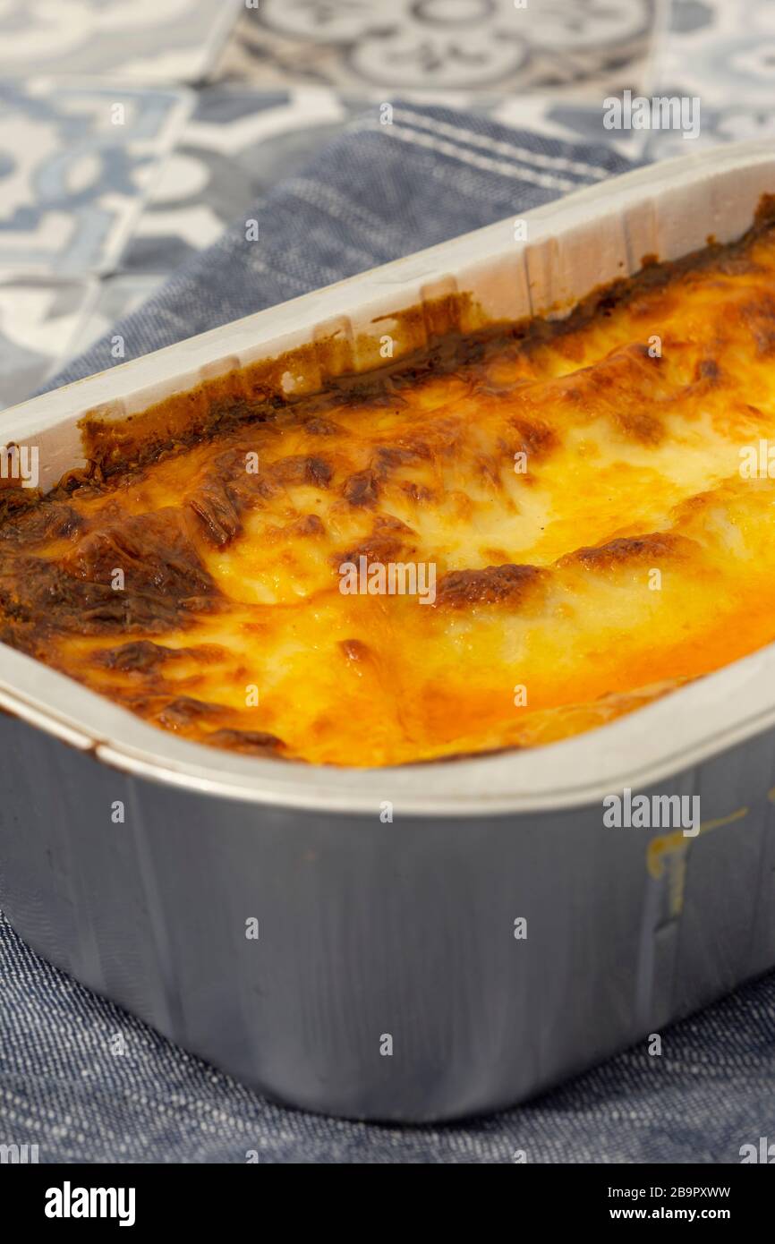 Beef Lasagne oder Lasagne zubereitete, tiefgefrorene Mahlzeit, die in einem Metallbackblech auf einem blauen Teehandel zubereitet wird. Fast-Food-Konzept Stockfoto