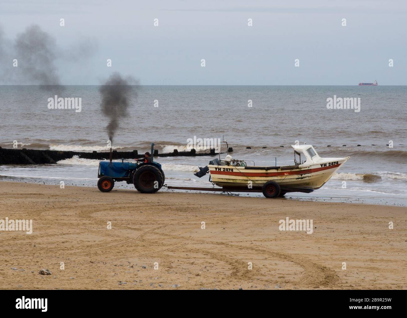 Cromer Fischer, der mit einem Trakor, Cromer, Norfolk, Großbritannien, das Boot am Strand hochzieht Stockfoto