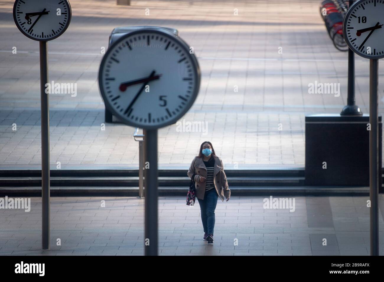 Eine Frau, die während der Hauptverkehrszeit eine schützende Gesichtsmaske trägt, spaziert in Canary Wharf, London, nachdem Premierminister Boris Johnson das Vereinigte Königreich in Sperrstellung versetzt hat, um die Ausbreitung des Coronavirus einzudämmen. Stockfoto