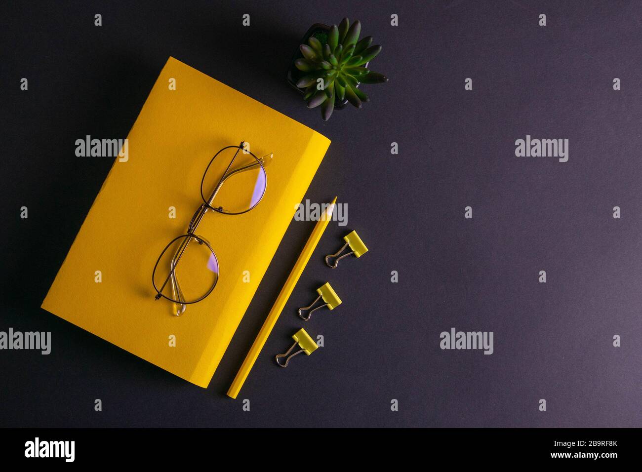Gelber Bleistift, gelbes Notizbuch und Brille, Stifte, Clip-Papier auf schwarzem Hintergrund Stockfoto