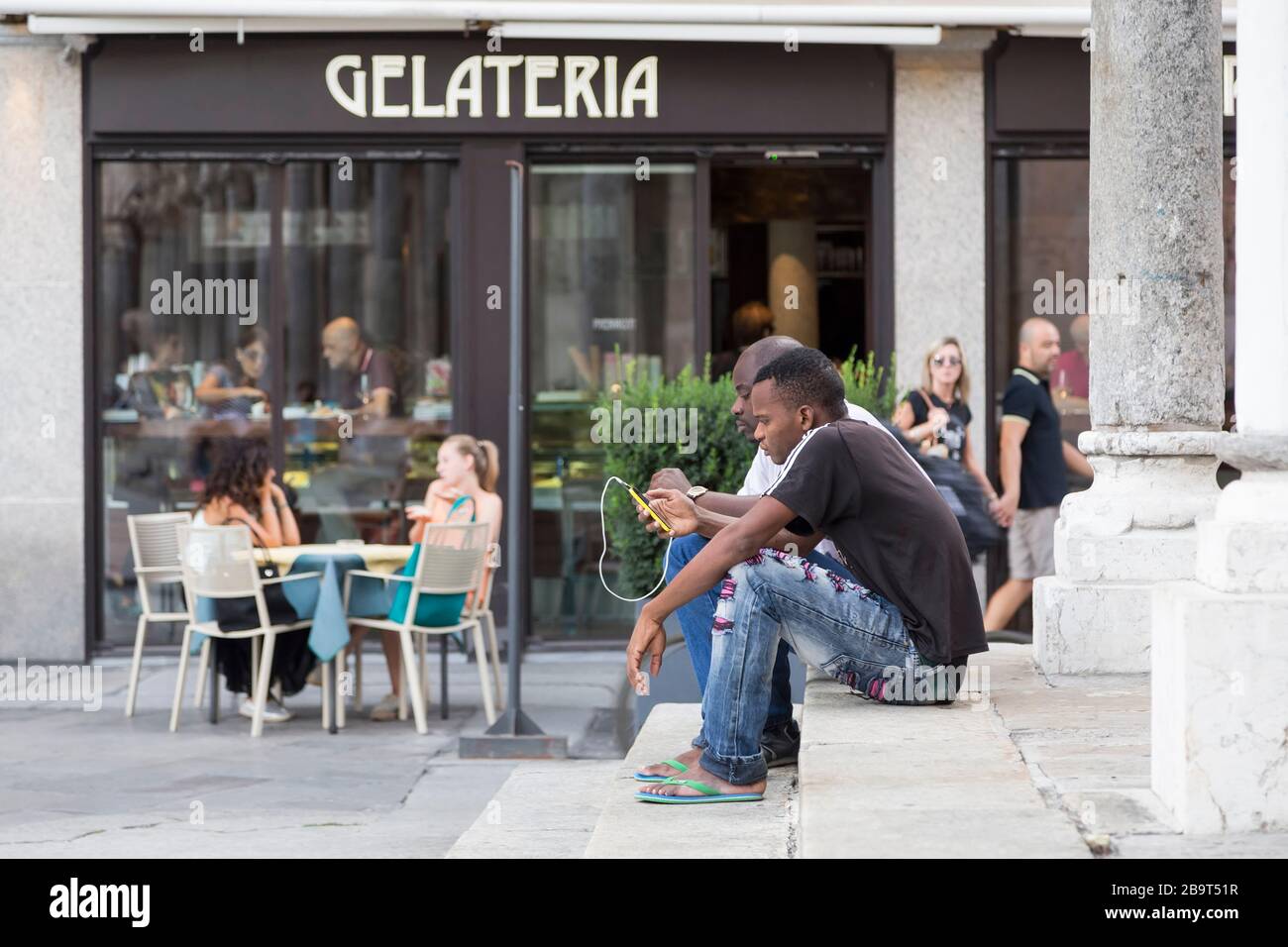 CREMES, ITALIEN - 2. SEPTEMBER 2015: Zwei schwarze Männer sitzen mit einem Telefon in den Händen auf den Stufen des Gebäudes. Cremona. Italien Stockfoto