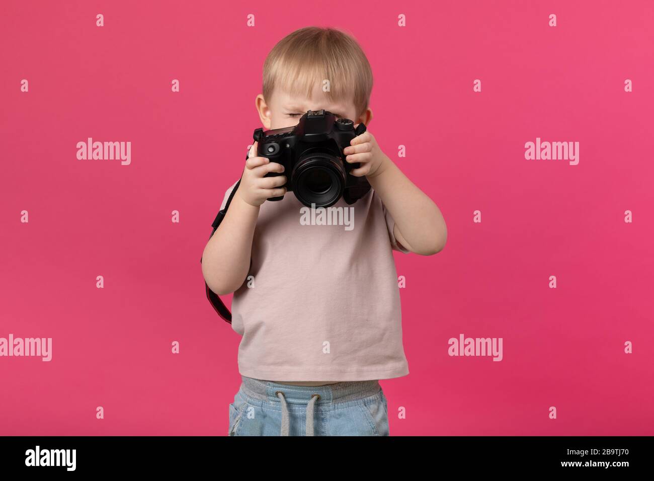 Ein kleiner Junge europäischer Erscheinung blonde Fotografien mit einer Kamera. Nahaufnahme des Studios auf einem rosafarbenen Hintergrund für Artikel über die Rekrutierung von Schulen Stockfoto
