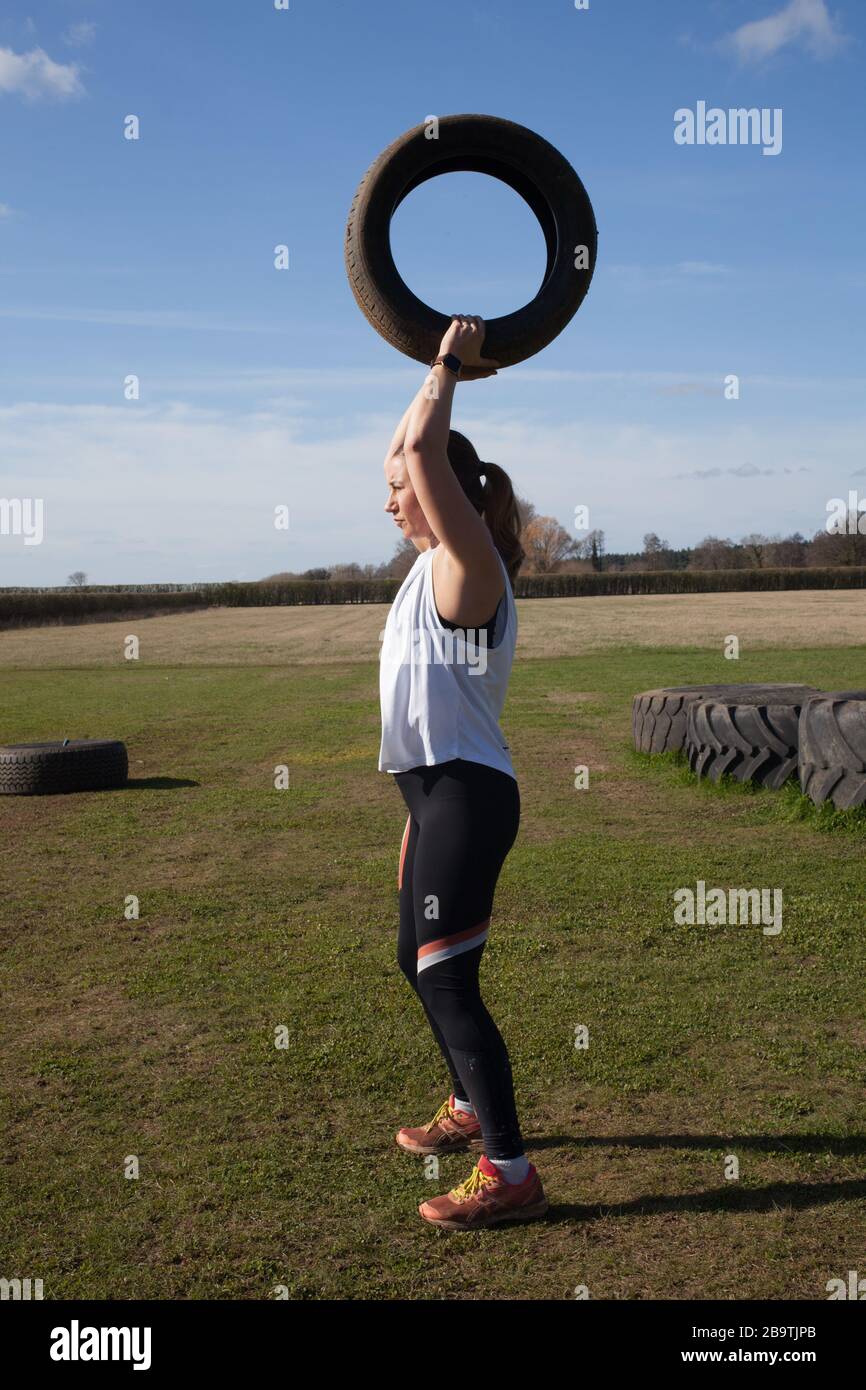 Eine Frau, die auf einer Farm in Großbritannien trainiert und dabei schwere Reifen abhebt Stockfoto