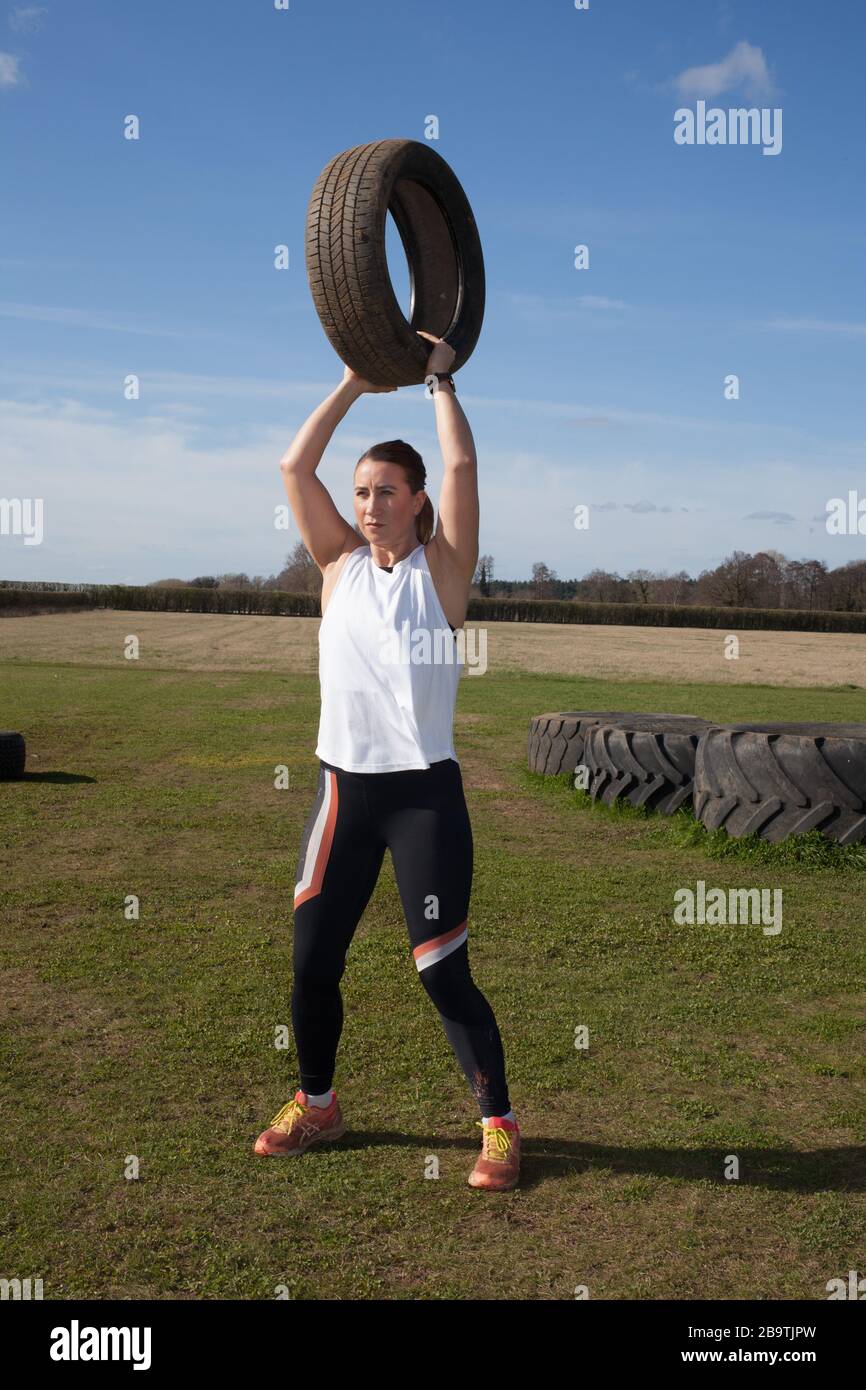 Eine Frau, die auf einer Farm in Großbritannien trainiert, indem sie schwere Reifen abhebt Stockfoto