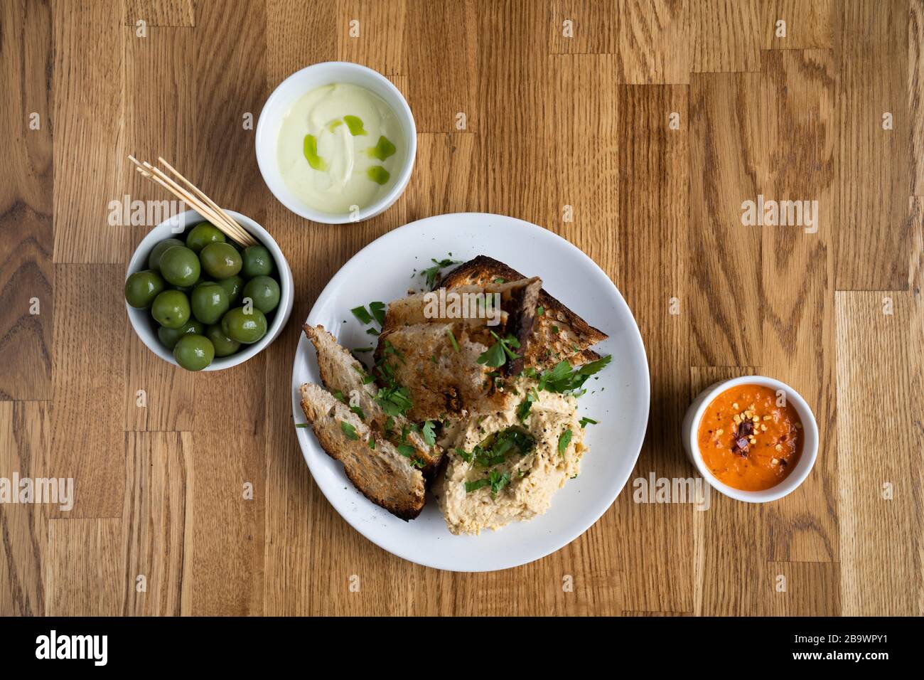 Italienische Beilagen in der Pizzeria - Harissa Chili Sauce, Oliven, Aioli mit Basilikumöl und Brot Stockfoto