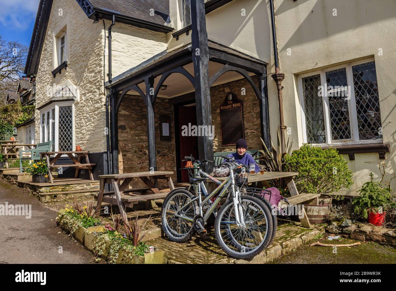 Ein Radfahrer, der sich ausruht und eine Pause außerhalb des Durant Arms Pub in Ashsprington im Dart Valley, South Hams, Devon, Großbritannien unternimmt. März 2018. Stockfoto
