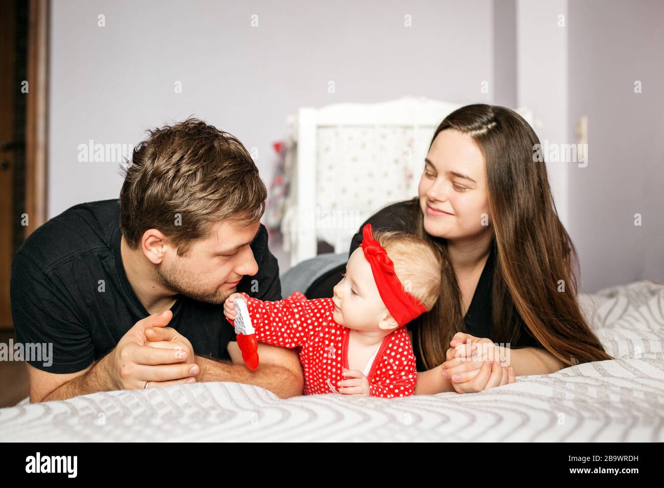 Mutter, Vater und Neugeborenes spielen zuhause. Rote Kleidung. Das Konzept der Familie, der Liebe, der Kinderbetreuung und des Wohnens. Stockfoto