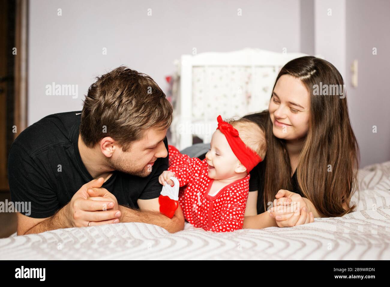 Eltern und ein neugeborenes Baby spielen zu Hause. Rote Kleidung. Das Konzept der Familie, der Liebe, der Kinderbetreuung und des Wohnens. Stockfoto