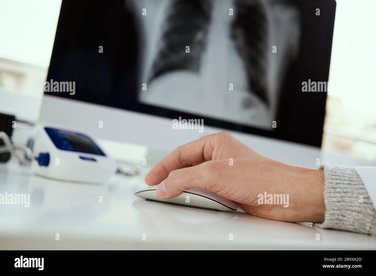 Nahaufnahme eines jungen Arztes, der an seinem Schreibtisch sitzt und einen Röntgenbild der Brust in seinem Computer überprüft Stockfoto