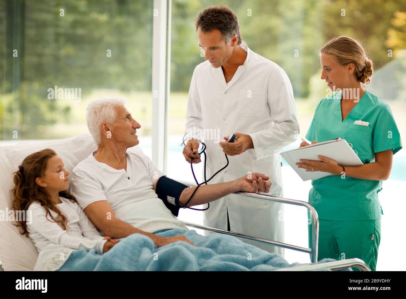 Der ältere Mann hat seinen Blutdruck genommen, während seine Enkelin neben ihm in einem Krankenhausbett liegt. Stockfoto