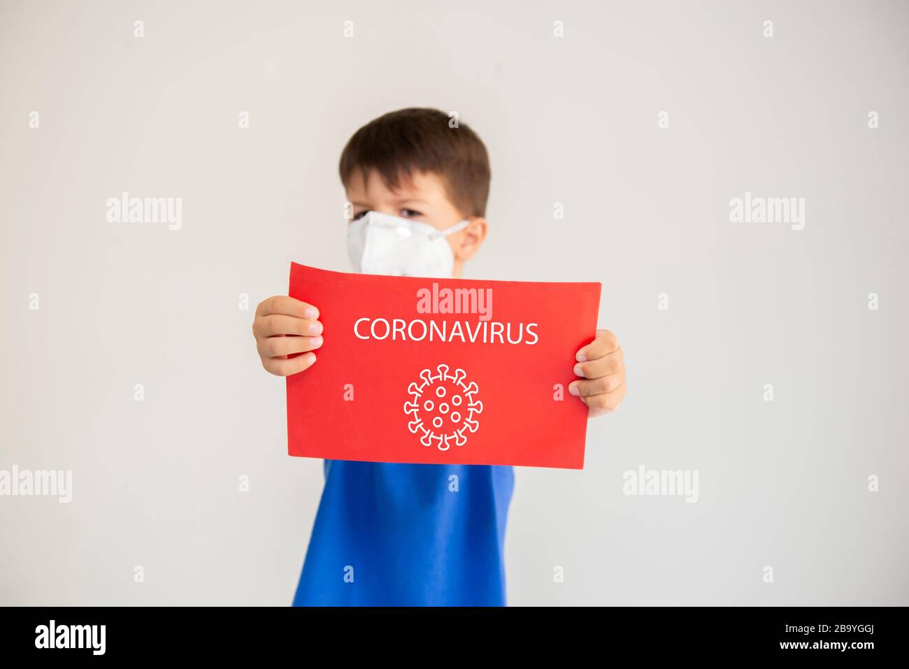 Kaukasischer Junge, der eine chirurgische Maske trägt, um Atemwegserkrankungen zu verhindern, die ein Papier mit dem Text: Coronavirus halten. Gesichtsmaske zum Schutz vor coron Stockfoto
