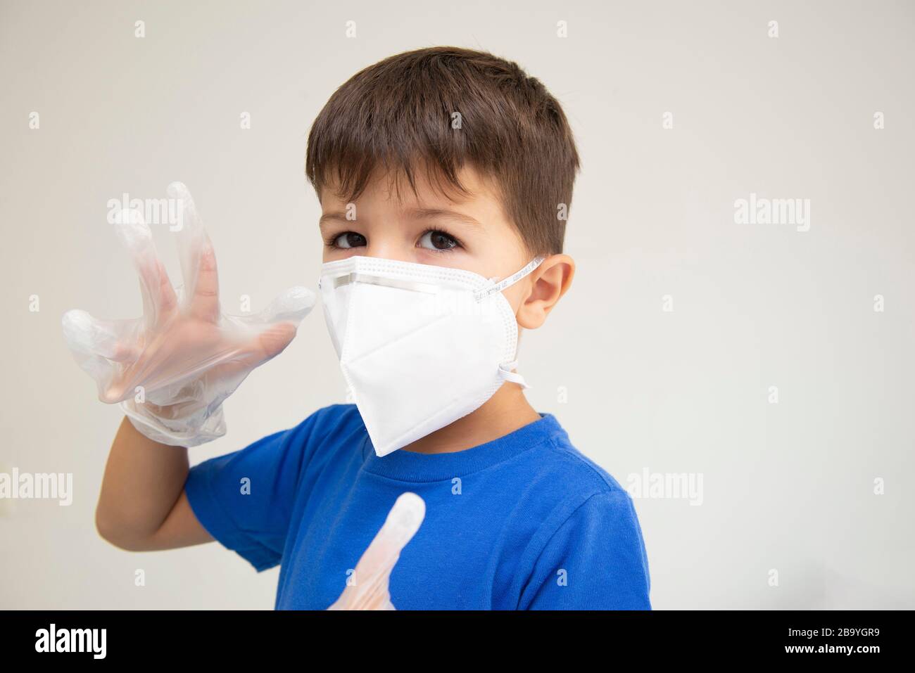 Kaukasischer Junge mit Maske und chirurgischen Handschuhen, die sich mit den Händen vor Atemwegserkrankungen schützen. Gesichtsmaske zum Schutz vor Ausblicken Stockfoto