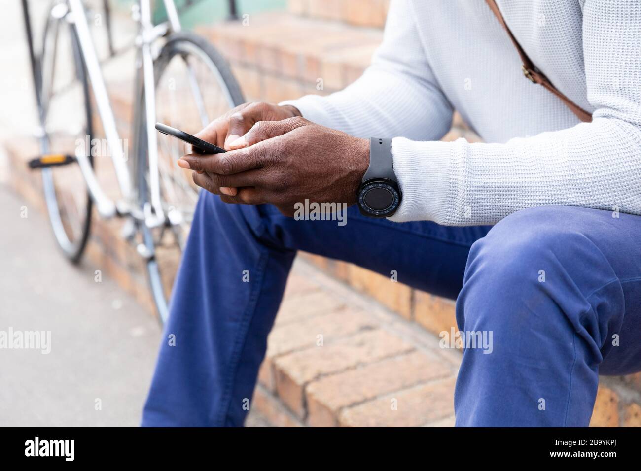 Afroamerikanischer Mann, der auf einer Treppe sitzt und sein Telefon benutzt Stockfoto