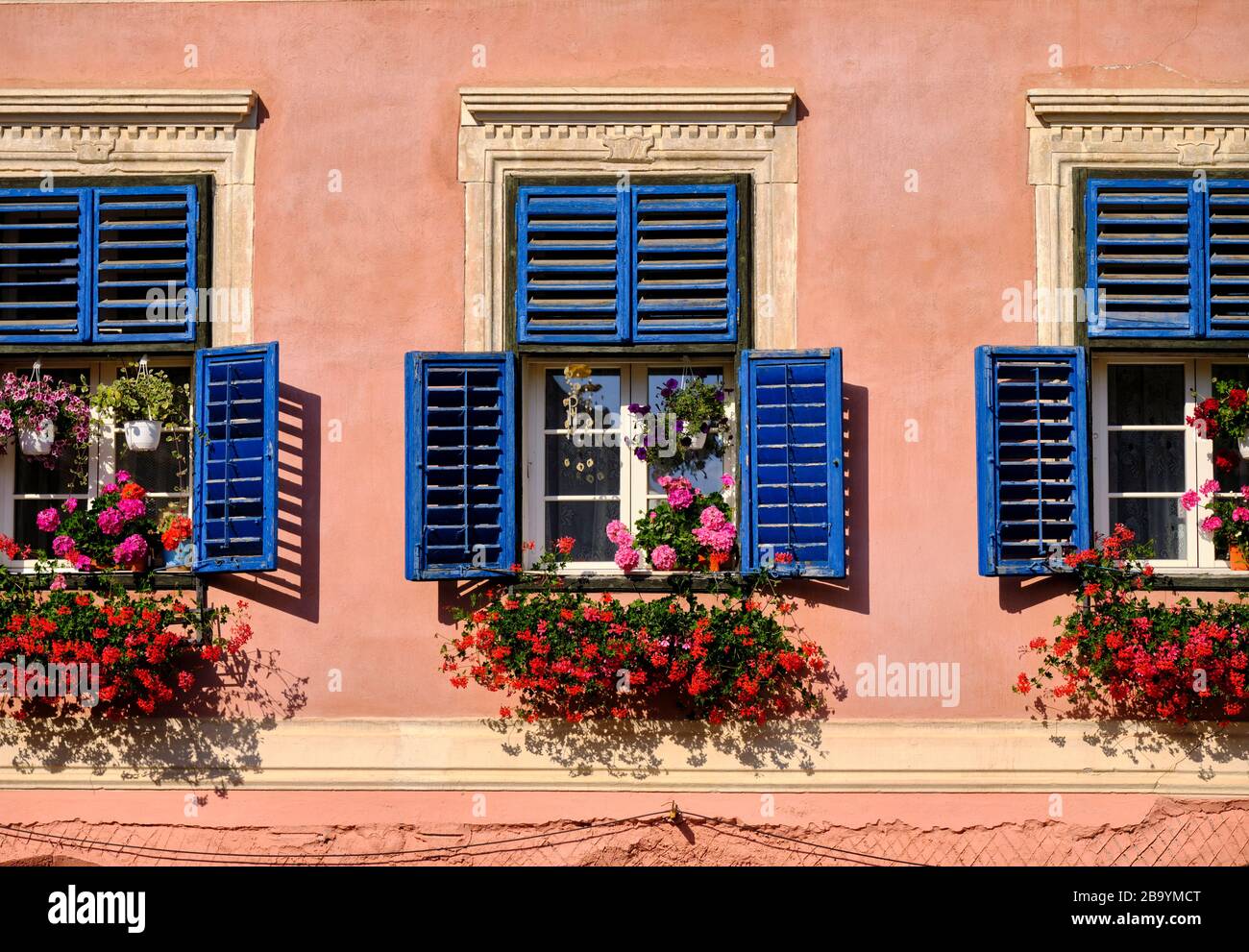 Oberes Bodenfenster mit blauen Blenden und Blumentöpfen und hängenden Körben. Stockfoto