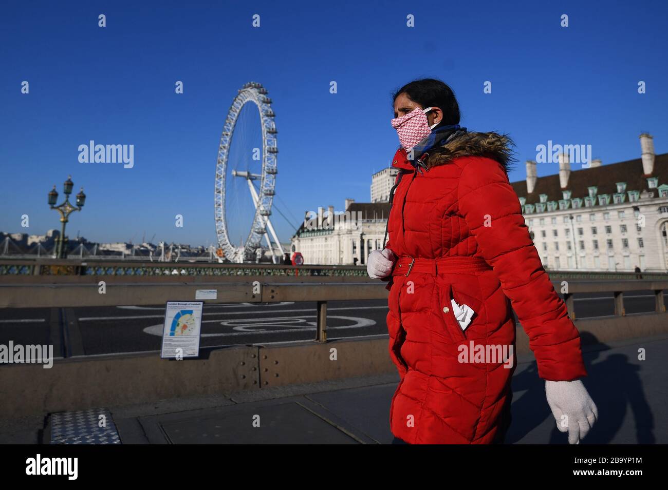 Eine Frau, die einen Facemask trägt, die auf einer ruhigen Westminster Bridge in London spazieren ging, nachdem Premierminister Boris Johnson die Entscheidung getroffen hatte, Großbritannien in eine Blockierung zu bringen, um die Ausbreitung des Coronavirus einzudämmen. Stockfoto