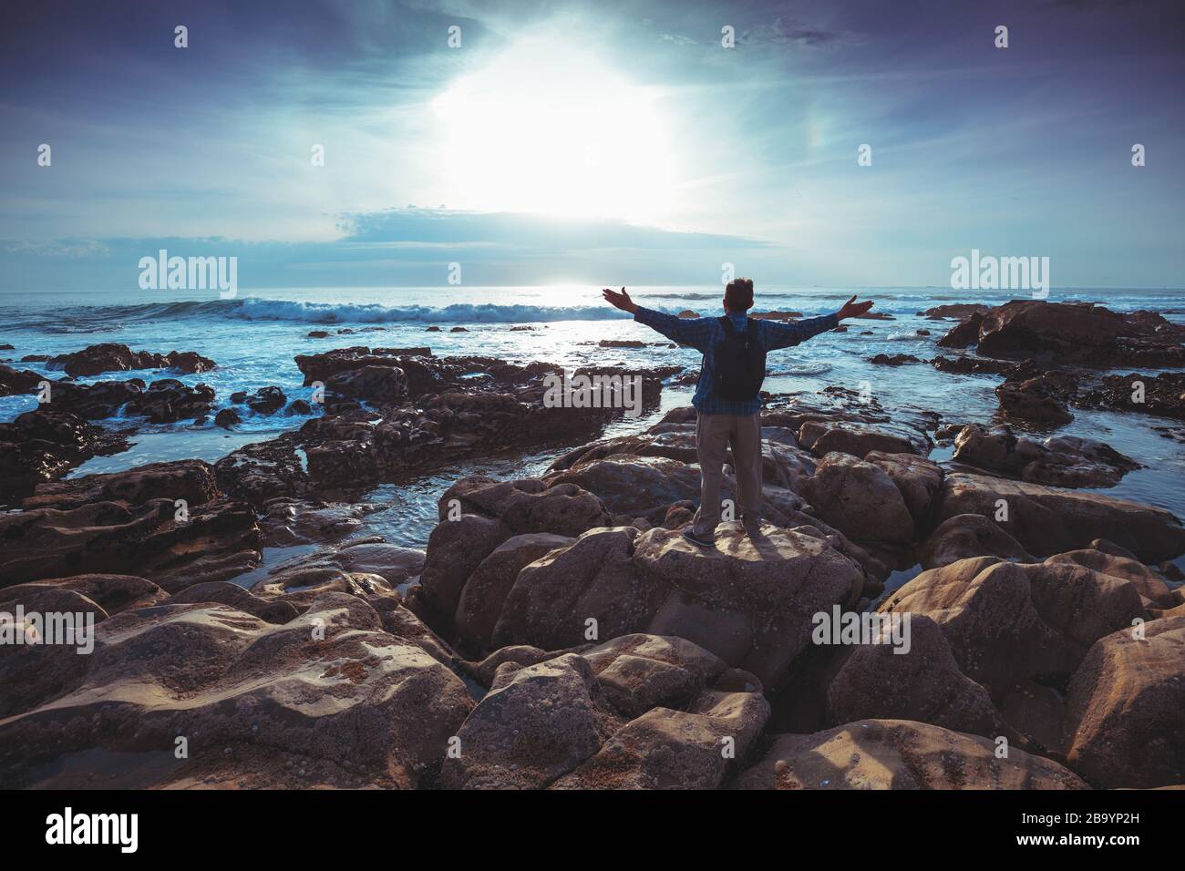 Am Abend seekapern. Felsige Küste bei Sonnenuntergang. Silhouette eines Mannes mit Händen in der Luft am Strand mit Blick auf den magischen Sonnenuntergang Stockfoto