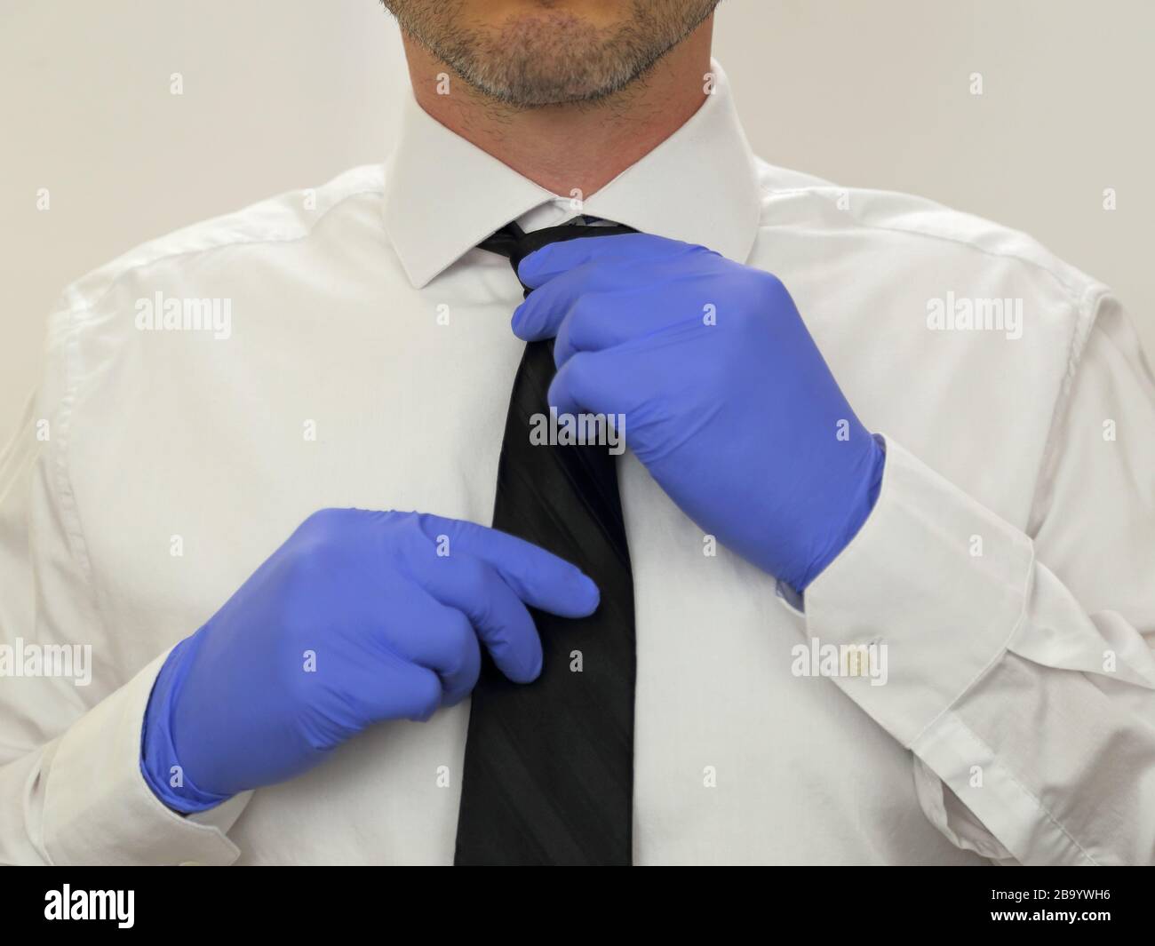 Ein Geschäftsmann passt eine schwarze Krawatte an, während er sterile blaue Nitrilgummihandschuhe und ein weißes Hemd in Nahaufnahme trägt. Stockfoto
