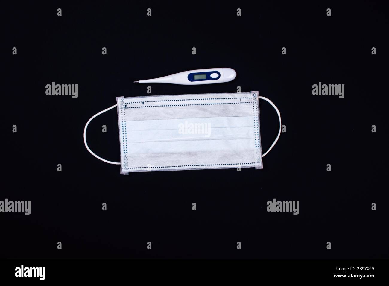 Thermometer und medizinische Gesichtsmaske auf schwarzem Hintergrund Stockfoto