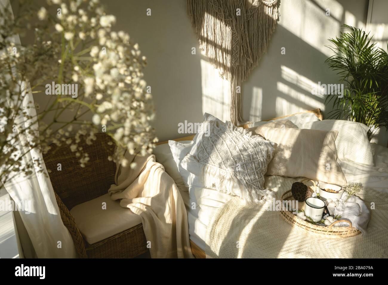 Gemütliches sonniges Schlafzimmer im Boho-Stil mit Licht und Schatten und einer Nahaufnahme weißer Zigeuner-Blumen. Authentisches, lebendes Interieur Stockfoto