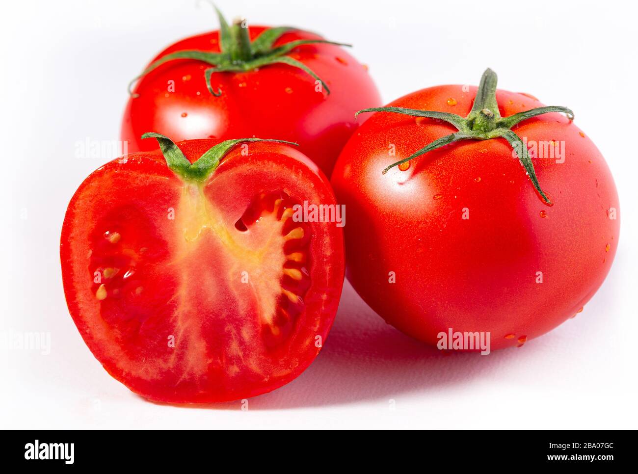 Zwei ganze und eine Hälfte frische rote Treibhaustomate auf einer weißen Oberfläche Stockfoto