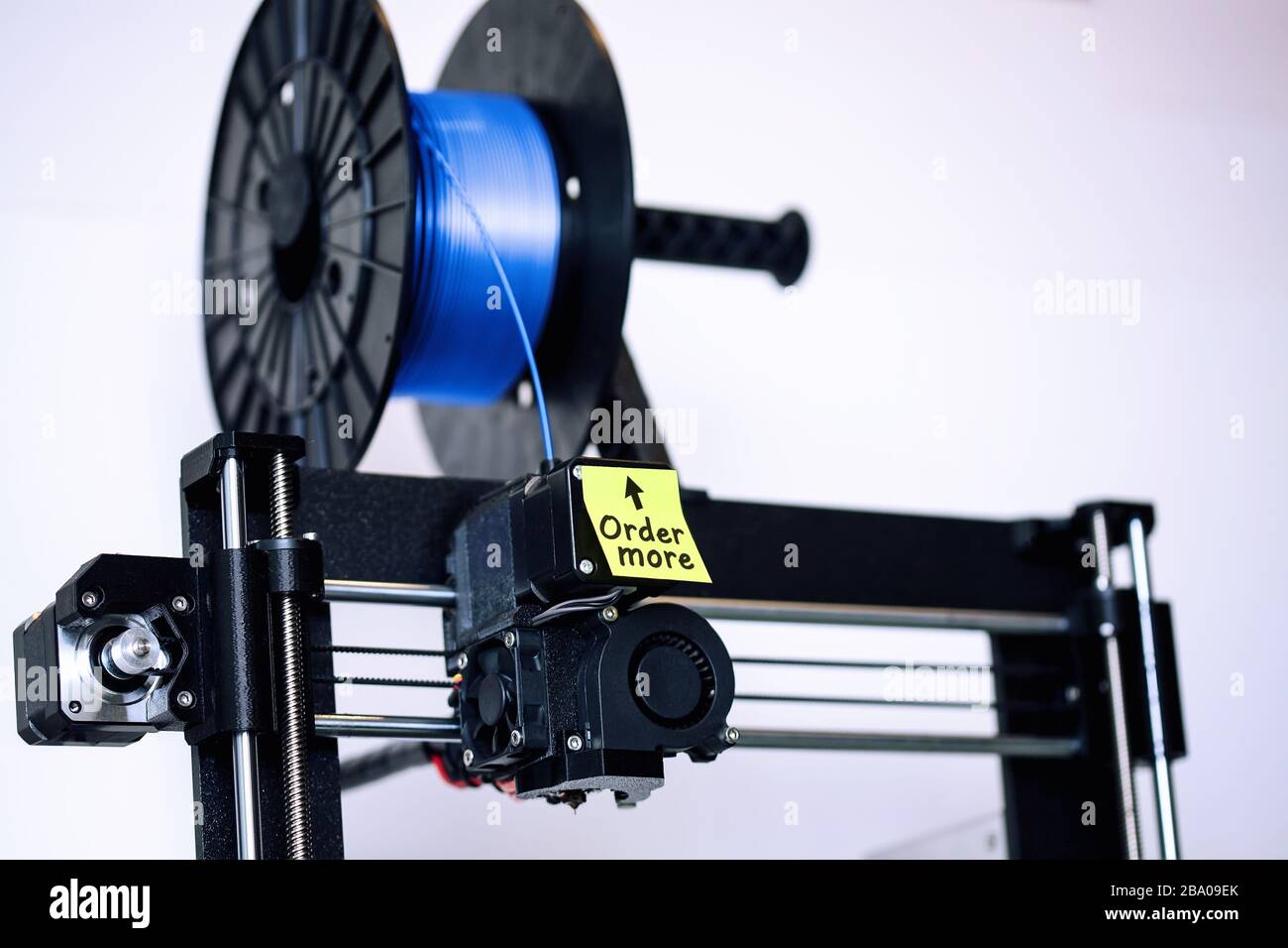 Ein 3D-Drucker im FDM-Stil mit einer Spule aus Filament, die niedrig läuft, und einer Haftnotiz zur Erinnerung, um mehr Silk-PLA-Glühfaden zu bestellen. Stockfoto
