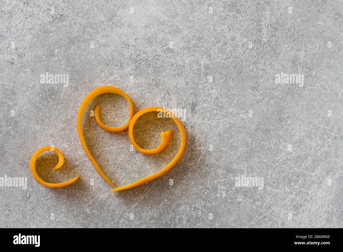 Orangefarbene Frucht geschälte Hautkräuseln auf steingrauem Grund. Abstrakte Herzform mit weichem Licht. Stockfoto