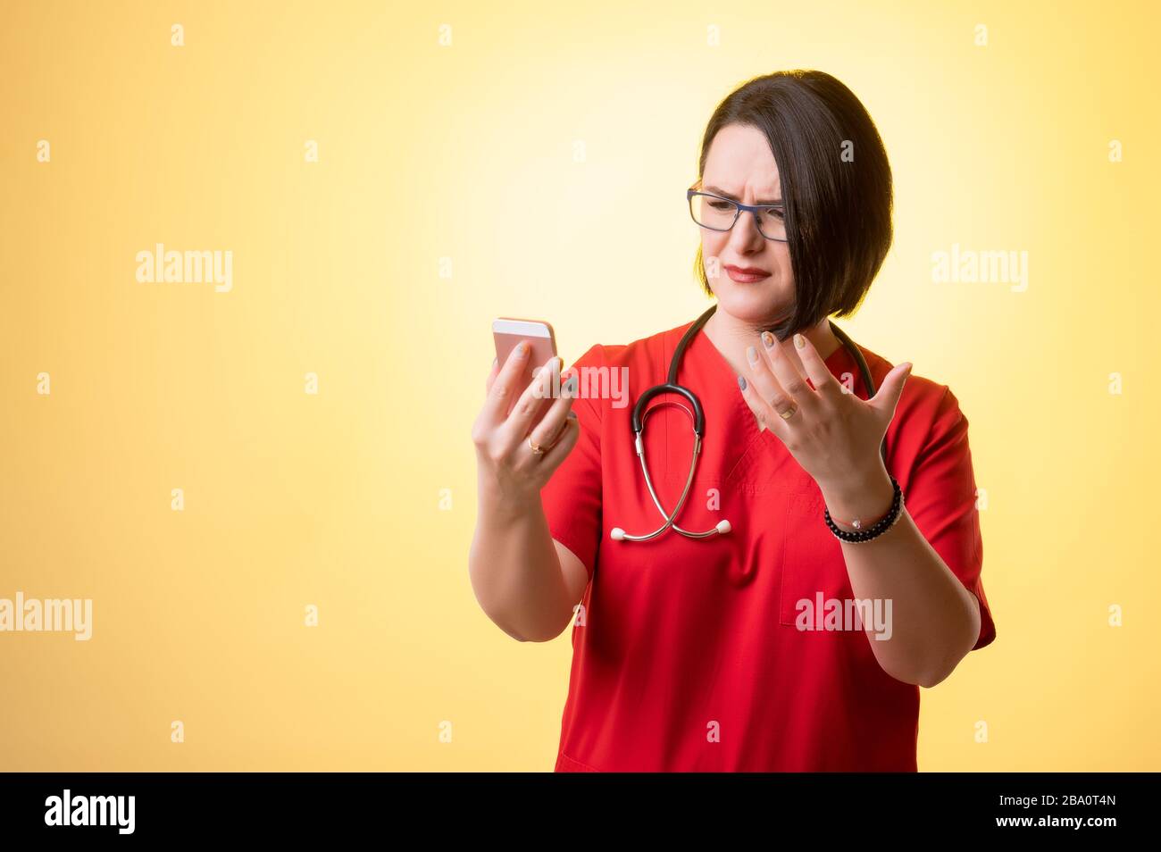 Porträt der schönen Frau Doktor mit Stethoskop mit roten Schruben, mit braunen Haaren, Smartphone halten, SMS schreiben, nervös schauen, auf einem y posieren Stockfoto