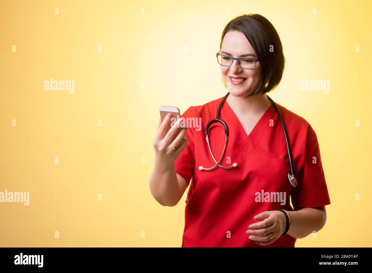 Porträt der schönen Frau Doktor mit Stethoskop mit roten Schruben, mit braunen Haaren, halten Smartphone, SMS-Nachrichten glückliches Gesicht auf einem y Stockfoto