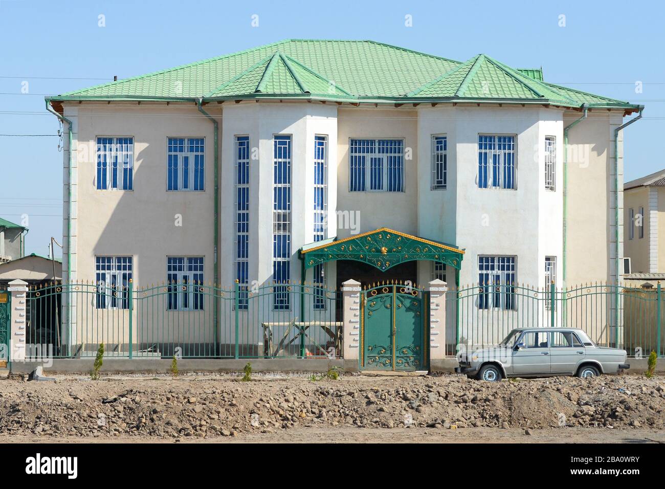 Außenansicht eines generischen Hauses für eine hochklassige turkmenische Familie mit zwei Etagen in Dashoguz, Turkmenistan. Grünes Dach und Zaun mit goldenen Verzierungen Stockfoto