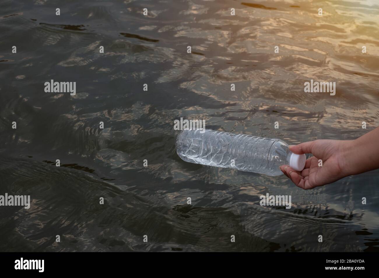Frau Hand, um die gebrauchte Plastikflasche auf dem Wasser in einem Kanal aufzunehmen Stockfoto